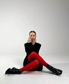 a woman sitting on the floor with her legs crossed and wearing red tights, black shoes