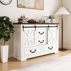 a living room with a white dresser and clock on the wall next to a potted plant