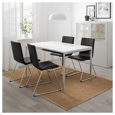 a white table with four black chairs and a brown rug in front of the window