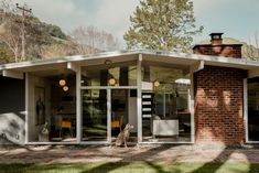 a dog sitting in front of a brick and glass house with an open patio area