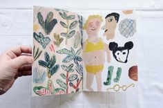 someone is holding an open book with drawings and plants on it in front of a white background