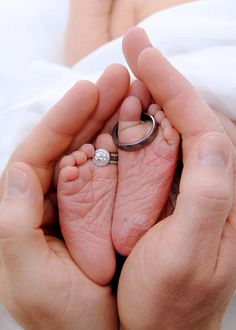 two hands holding a baby's feet with a wedding ring on top of it