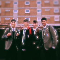 four young men in suits and ties posing for a photo with the building behind them