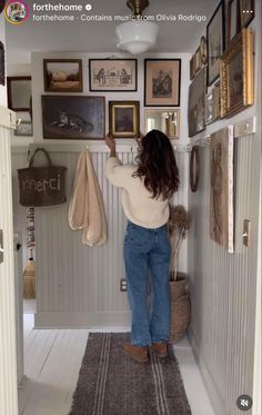 a woman is standing in the hallway looking at pictures on the wall above her head