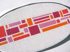 a close up of a cross stitch pattern on a piece of white fabric with orange and pink squares