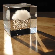 a clear box with some white clouds in it sitting on a wooden table next to a window