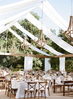 an outdoor wedding reception with white draping and chandeliers hanging from the ceiling