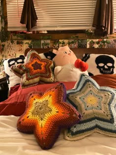 three crocheted pillows on a bed with skulls in the window sill behind them