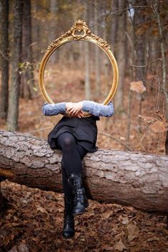 a woman sitting on top of a log in the woods with a mirror over her head