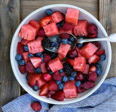 a bowl filled with watermelon, blueberries and raspberries on top of a wooden table