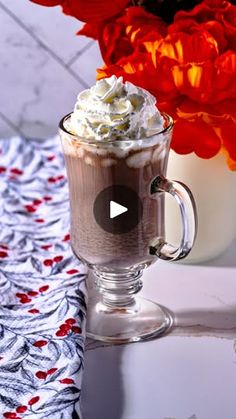 there is a cup of hot chocolate with whipped cream on top and flowers in the background