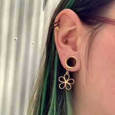 a close up of a person with green hair wearing gold earring and piercings