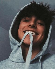 a young man wearing a blue hoodie and holding a toothbrush in his mouth