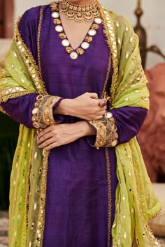 A striking ensemble, this purple raw silk sharara set showcases exquisite mirror work on the neckline and sleeves of the tunic, exuding elegance and charm. Paired with matching pants and a contrasting lime green organza dupatta, this outfit beautifully balances richness and vibrancy, making it a perfect choice for festive celebrations and special events. Lehnga Kurta Design, Mirror Work Suits Design Pakistani, Short Kurti With Garara, Contrast Dupatta Suits, Mirror Work Sleeve Design, Desi Look Outfits, Heavy Dresses Indian Suits, Purple Matching Colors Outfit, Contrast Suit Design