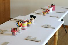 several pencils and markers are lined up on a long white table with wooden legs