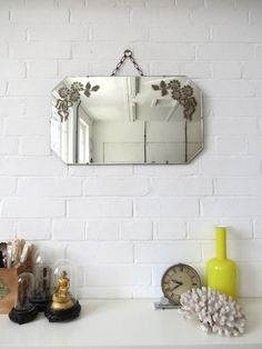 a mirror hanging on the side of a white brick wall next to a clock and other items