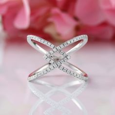 a white gold diamond cross ring on a table with pink flowers in the foreground