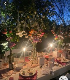 a table set for dinner with candles and flowers in vases on the table, surrounded by greenery