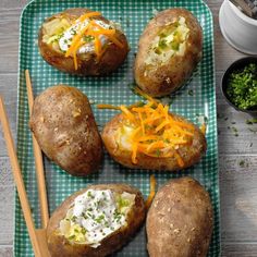 four baked potatoes on a green plate with chopsticks