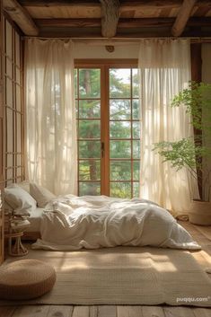 a bed sitting under a window next to a wooden floor covered in white sheets and pillows