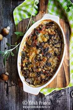 a casserole dish with mushrooms and cheese on a wooden table next to green napkins