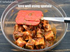 a bowl filled with tofu and sauce on top of a wooden table next to a knife