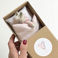 a hand holding a box with a stuffed animal in it's lap and the packaging is open