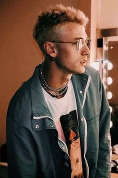 a young man wearing glasses and a neck tie in front of a mirror with lights behind him