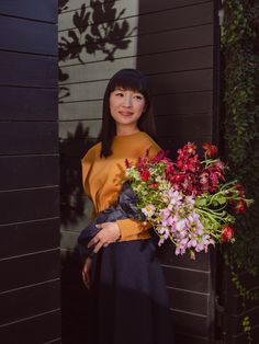 a woman standing in front of a house holding a bouquet of flowers