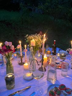 a table is set with candles, plates and wine glasses for an outdoor dinner party