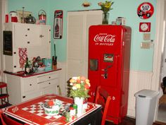 an old fashioned coca - cola machine is in the corner of a kitchen with red table and chairs