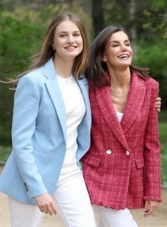 two women standing next to each other in white pants and pink blazer jackets smiling at the camera