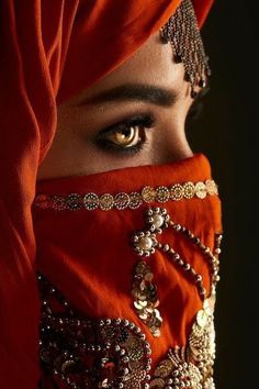 a woman wearing a red veil with jewels on her head and eyes covered by an orange cloth