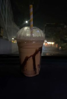 a cup with a straw in it sitting on a table next to a window at night