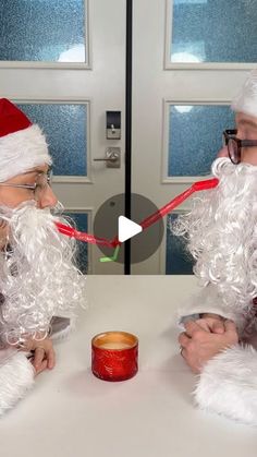 two men dressed as santa claus sitting at a table with a candle in front of them