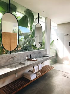 a bathroom with two sinks and mirrors on the wall next to each other in front of plants