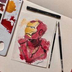 a drawing of iron man on paper next to paintbrushes and watercolor paints