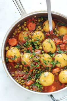 a pot filled with stew and vegetables on top of a table next to utensils