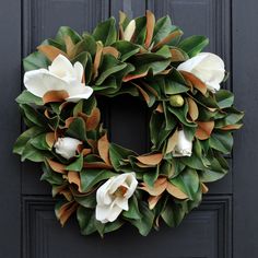 a wreath with white flowers is hanging on a black front door and has green leaves around it