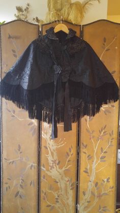 "One of a kind amazing Victorian black brocade embroidered fringed cape! This awesome cape has embroidered collars and across shoulders and front, the embroidery is a light black/ brown colour. There is a large black ribbon band that comes around the back of neck and down front sides with ribbon flowers at the ends and ties up the front, the ribbon is torn in places, could be easily replaced if you have a good seamstress! The black crochet and fringing is amazing! There are metal hook and eye fa Black Capelet For Costume, Elegant Black Capelet For Costume, Elegant Black Cape For Costume, Black Shawl Cape For Festival, Black Bohemian Cape For Festivals, Bohemian Black Cape For Festival, Black Evening Cape, Traditional Black Cape For Fall, Black Capelet For Party