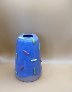 a blue vase with sprinkles on it sitting in front of a wall