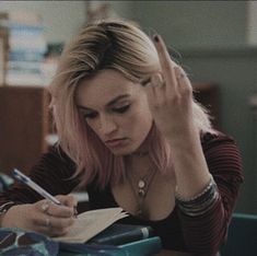 a woman sitting at a desk writing on a piece of paper with a pen in her hand