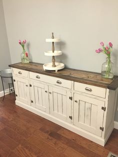 two vases with flowers sit on top of a white buffet table in a living room