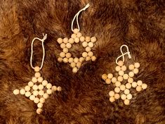 three small white beads hanging from strings on a brown fur covered surface with two pairs of earrings in the shape of snowflakes