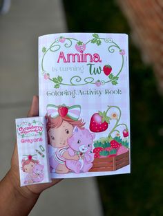 a person holding up a children's coloring book with an animal and strawberry on it