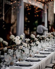 a long table is set with white flowers and place settings for an elegant dinner party