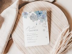 a white and blue floral bridal shower card on a wooden plate next to some feathers