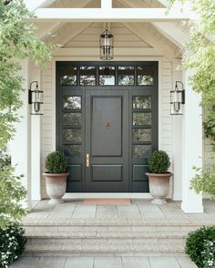 a black front door with two planters on the steps and an entry way leading up to it