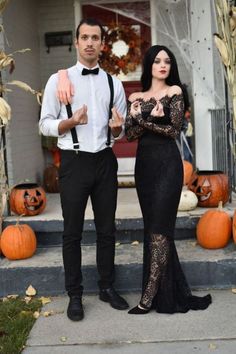 a man and woman dressed up for halloween standing in front of a house with pumpkins