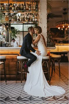 a pregnant woman sitting on top of a man's lap in front of a bar